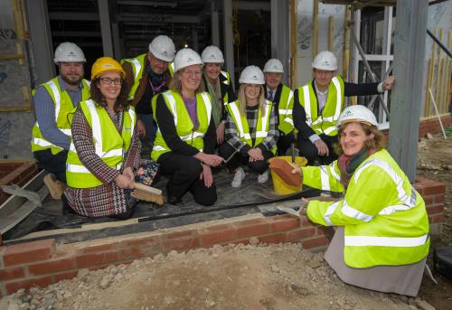 LEP & AECC staff in high vis/hard hats laying final brick at integrated rehab centre topping out ceremony