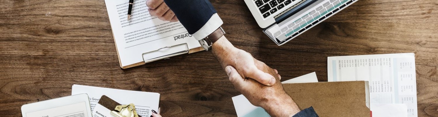 2 men shaking hands over a desk of papers 