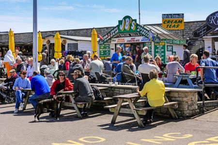 People sitting at picnic tables eating fast food at West Bay in Dorset, UK 